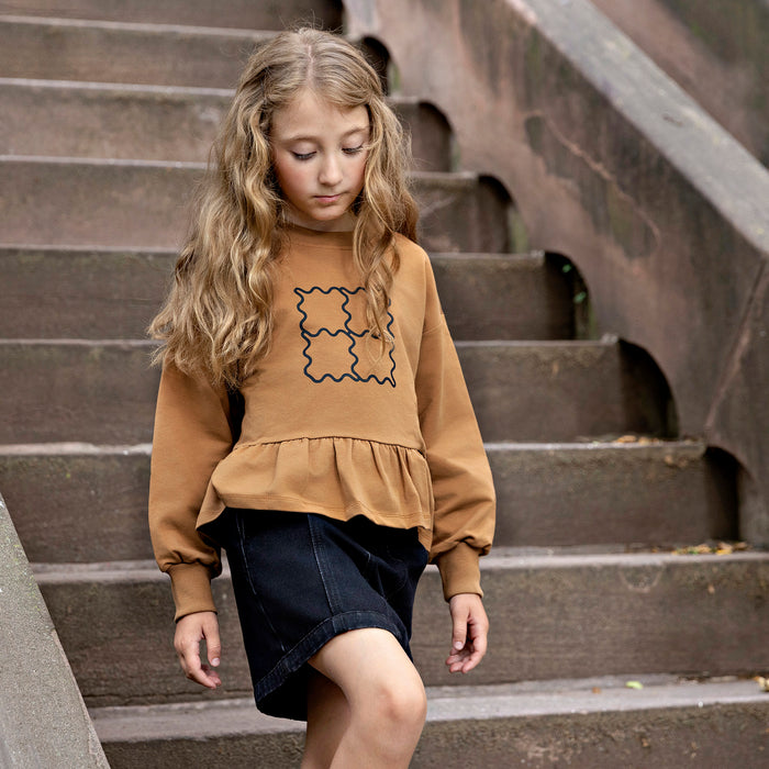 Girl wearing a Rooie and Friends caramel ruffle sweatshirt with a black denim skirt