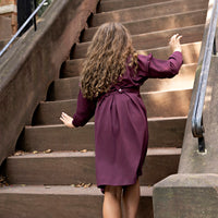 Girl wearing a Rooie and Friends mauve pleated pinafore dress over a matching ruffle sweatshirt