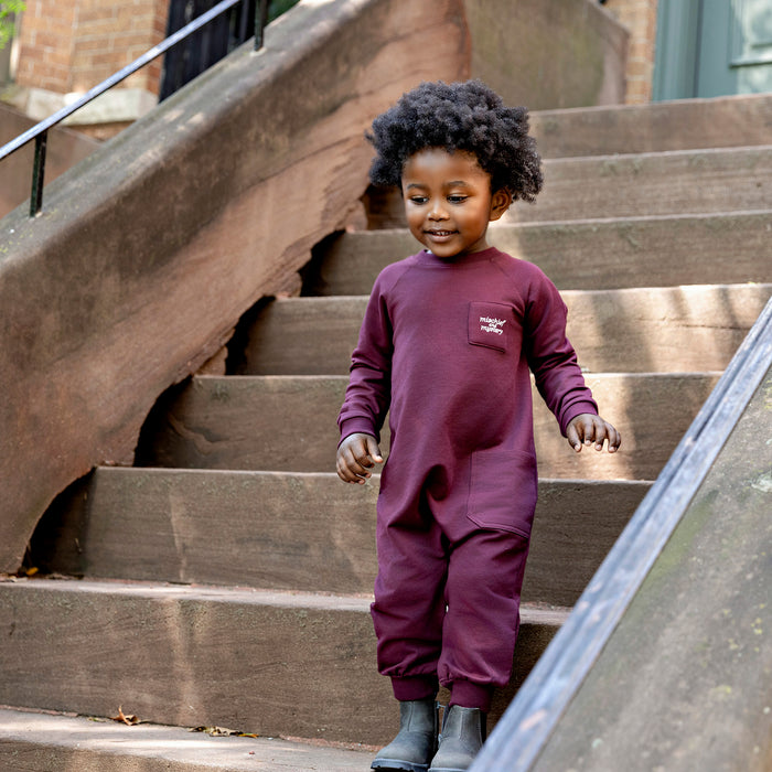 Toddler wearing a Rooie and Friends mauve boiler suit on brownstone steps