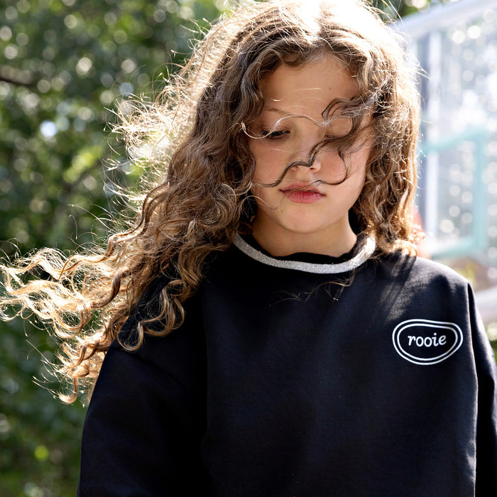 Girl wearing a Rooie and Friends black sweatshirt with silver trim at a basketball court