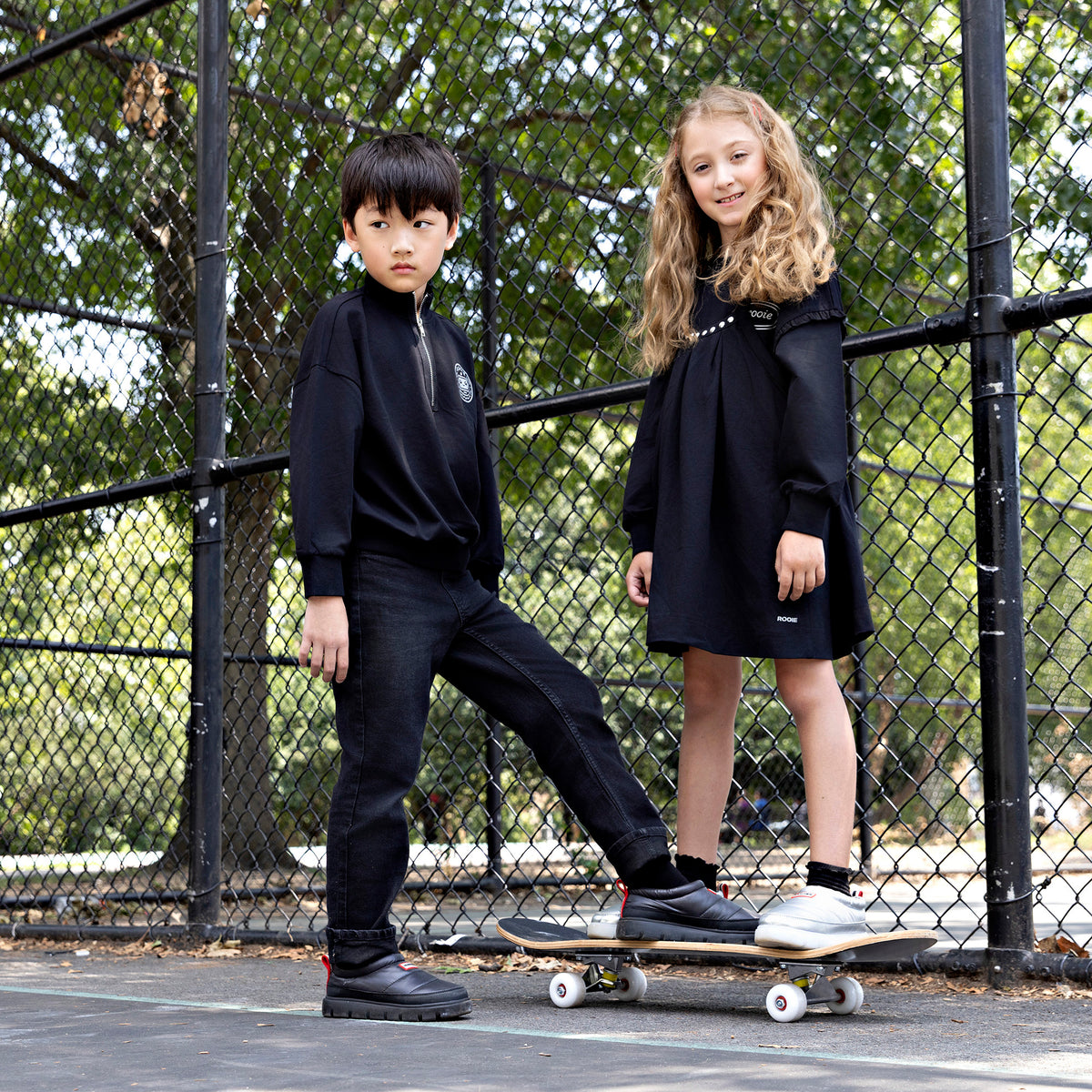 Girl wearing a Rooie and Friends black studded pinafore dress over a black long-sleeve top