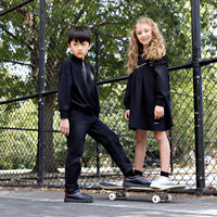 Girl wearing a Rooie and Friends black studded pinafore dress over a black long-sleeve top