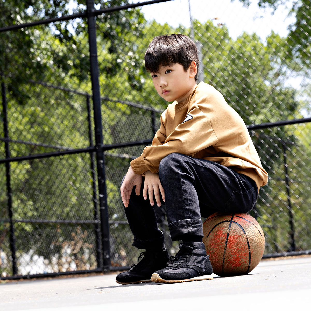 Boy wearing a Rooie and Friends caramel patch sweatshirt at a basketball court